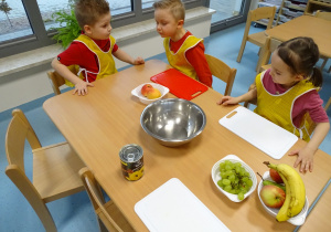 dzieci siedzą przy stoliku z owocami